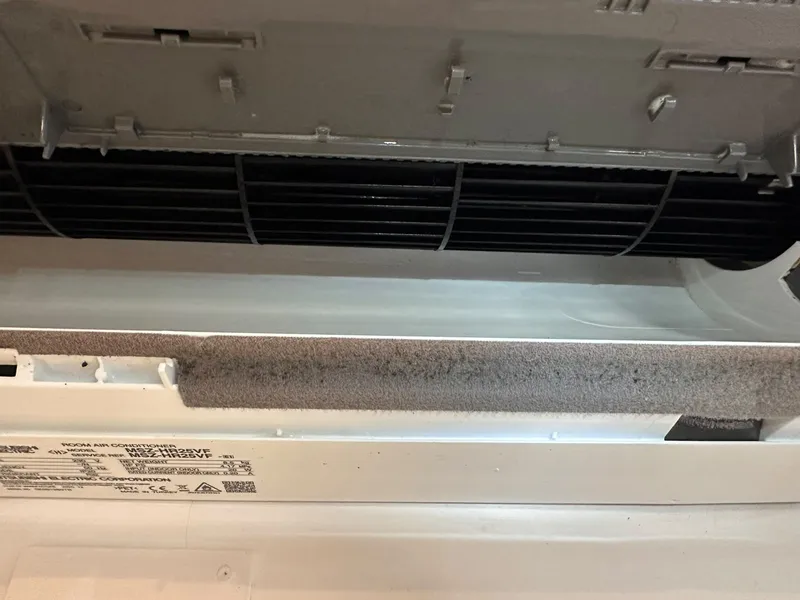 Interior de uma unidade de ar condicionado com camada escura de sujidade depositada na turbina e na saída de ar